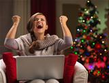 Happy woman with laptop rejoicing success in front of Christmas tree