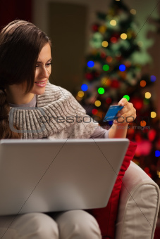 Happy woman in front of Christmas tree making online purchases