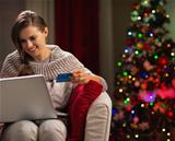 Happy woman with laptop and credit card in front of Christmas tree