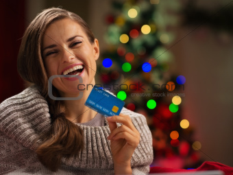 Smiling woman in front of Christmas tree holding credit card