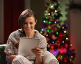 Happy woman looking in tablet PC in front of Christmas tree