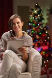 Happy woman in front of Christmas tree holding tablet PC