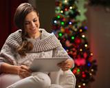 Happy woman sitting with tablet PC in front of Christmas tree