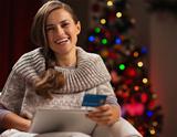 Smiling woman with tablet PC and credit card in front of Christmas tree
