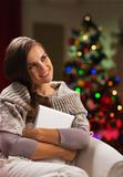 Happy woman in chair in front of Christmas tree hugging tablet PC