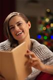 Happy woman in front of Christmas tree reading book