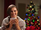 Smiling young woman with cup of hot chocolate in front of Christmas lights