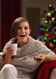 Surprised young woman with cup of hot beverage looking TV