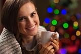 Happy young woman enjoying cup of hot chocolate in front of Christmas lights