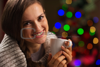 Happy young woman enjoying cup of hot chocolate in front of Christmas lights