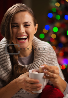 Happy young woman taking out marshmallow from cup of hot chocolate