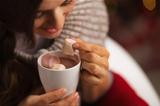 Closeup on woman taking out marshmallow from cup of hot chocolate