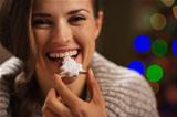 Happy woman eating Christmas cookie in front of Christmas lights
