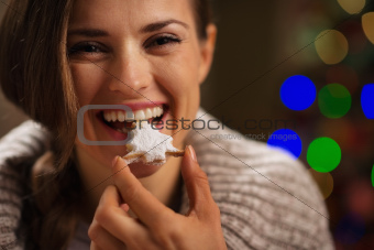 Happy woman eating Christmas cookie in front of Christmas lights