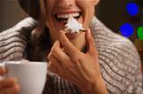 Closeup on happy woman eating Christmas cookie in front of Christmas lights
