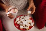Closeup on woman eating Christmas cookie and drinking hot chocolate with marshmallows