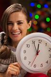 Portrait of smiling woman showing clock in front of Christmas lights