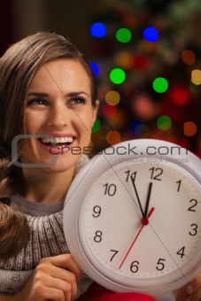 Portrait of happy woman showing clock in front of Christmas lights