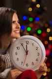 Portrait of happy woman showing clock in front of Christmas lights
