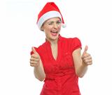 Happy young woman in Christmas hat winking and showing thumbs up