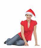 Smiling young woman in Santa hat sitting on floor