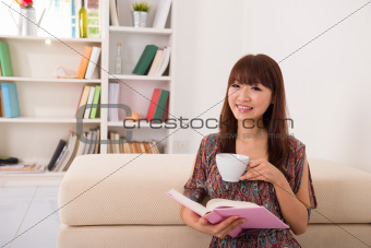 happy asian girl reading on sofa 
