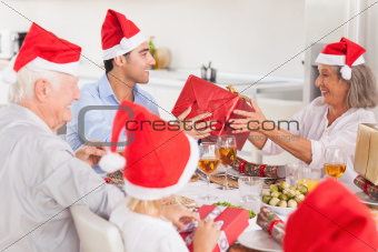 Happy family exchanging gifts at christmas time around the dinner table