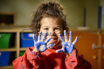 Happy little girl painting with hands in kindergarten