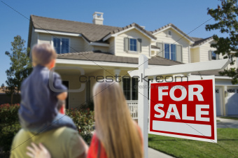 Young Family Looking at a Beautiful New Home with a For Sale Real Estate Sign in Front.