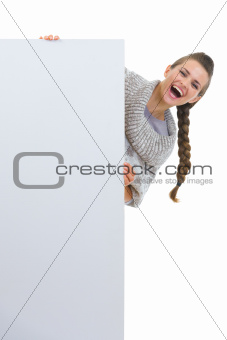 Happy woman in sweater looking out from blank billboard