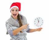Surprised woman in Santa hat pointing on clock