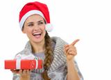 Woman in Santa hat holding Christmas gift and pointing on copy space