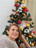 Dreaming woman in sweater sitting in front of Christmas tree