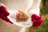 Woman Wearing A Sweater and Seasonal Red Mittens Holding A Plate of Pecan Pie with Peppermint Sticks.