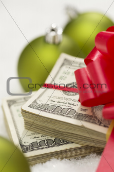 Stack of One Hundred Dollar Bills with Red Bow Near Green Christmas Ornaments on Snow Flakes.
