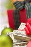 Stack of One Hundred Dollar Bills with Red Bow Near Green Christmas Ornaments and Wrapped Gift Box on Snow Flakes.