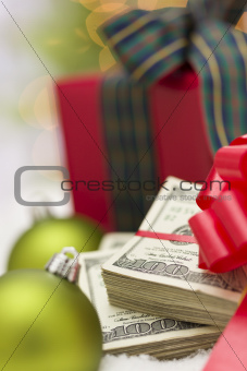 Stack of One Hundred Dollar Bills with Red Bow Near Green Christmas Ornaments and Wrapped Gift Box on Snow Flakes.