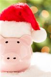 Pink Piggy Bank Wearing Red and White Santa Hat on Snowflakes with Abstract Green and Golden Background.