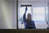 Professional maid cleaning and wiping window in office with soap