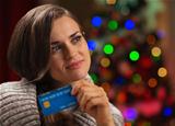 Portrait of thoughtful woman with credit card in front of Christmas lights