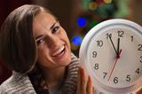 Portrait of smiling young woman showing clock in front of Christmas lights
