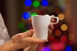 Closeup on cup with hot beverage in front of Christmas lights
