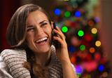 Smiling young woman speaking mobile phone in front of Christmas lights