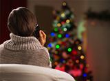 Young woman calling mobile in front of Christmas tree. Rear view