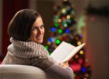 Happy young woman reading book in front of Christmas tree