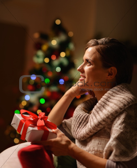 Dreaming young woman sitting chair with Christmas present box