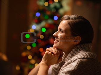 Dreaming young woman sitting chair in front of Christmas tree