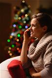 Young woman sitting chair and making phone call in front of Christmas tree