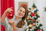 Happy young woman holding Christmas ball in front of Christmas tree
