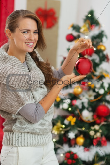 Happy young woman holding Christmas ball near Christmas tree